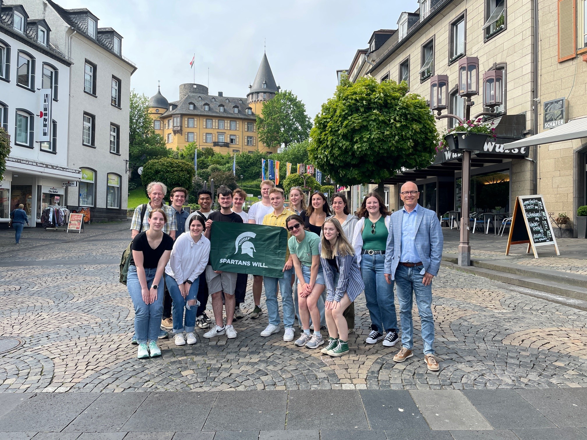 Eine Gruppe Studierende stehen auf dem Marktplatz zusammen - es wird eine Fahne hochgehalten