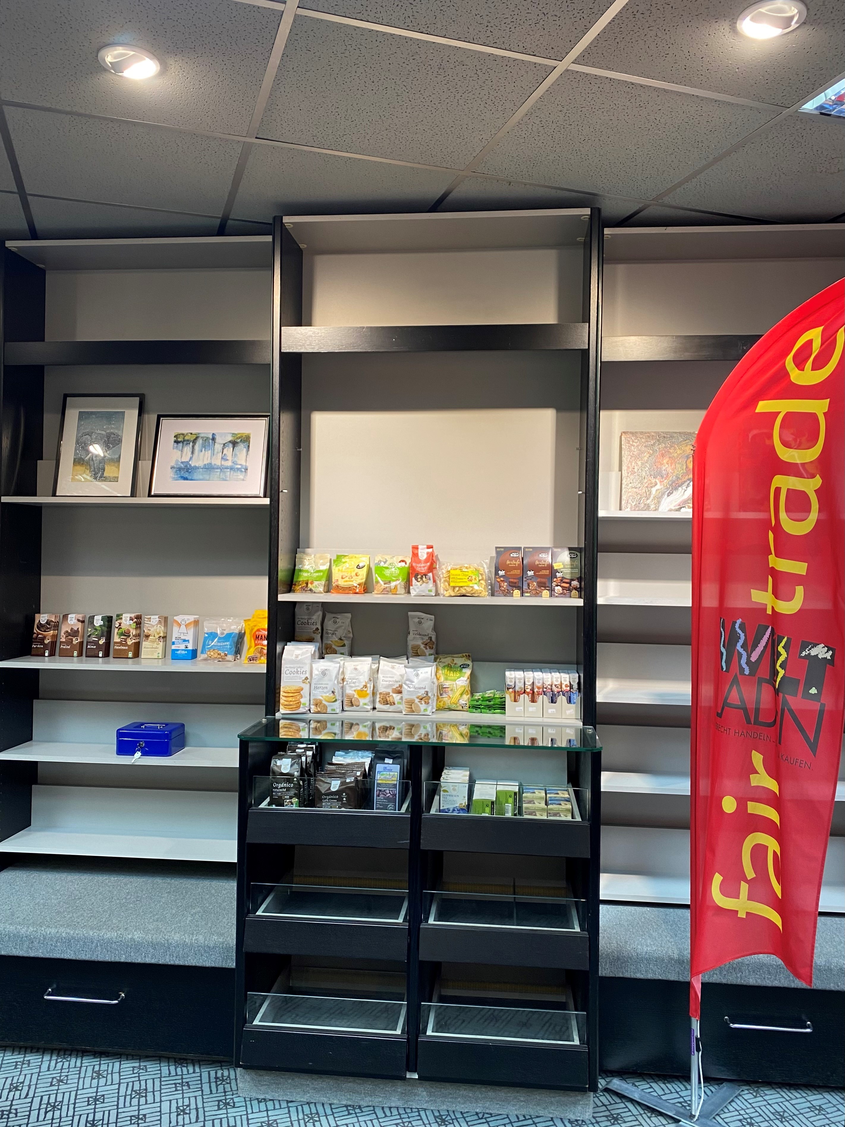 Eine VItrine mit fairen Produkten vor einem Bücherregal, daneben ein roter Aufsteller