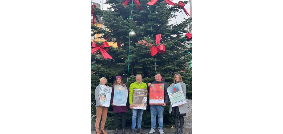 Fünf Personen stehen mit Plakaten vor einem Weihnachtsbaum