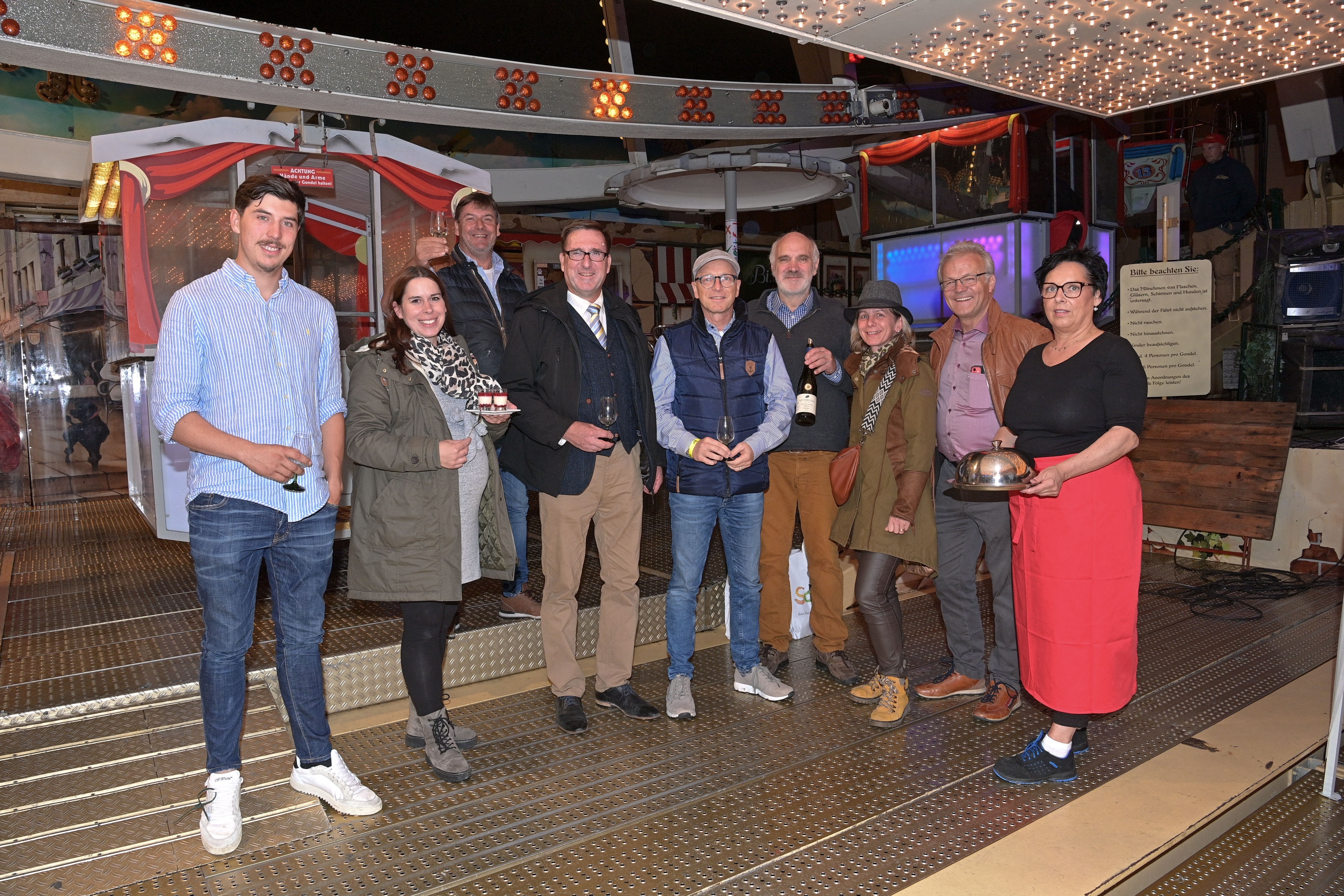 9 Personen stehen vor dem Eingang des Riesenrads und haben Wein, Weingläser und Essen in der Hand