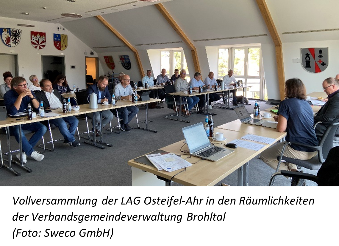 Personen sitzen an Tischen in einem Versammlungssaal und tauschen sich aus