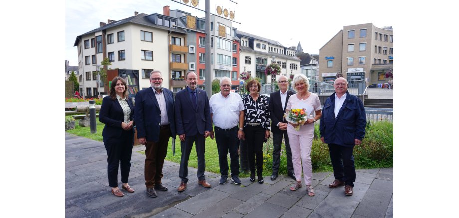 8 Personen stehe vor dem Rathaus - eine Dame hält einen Strauß Blumen in den Händen