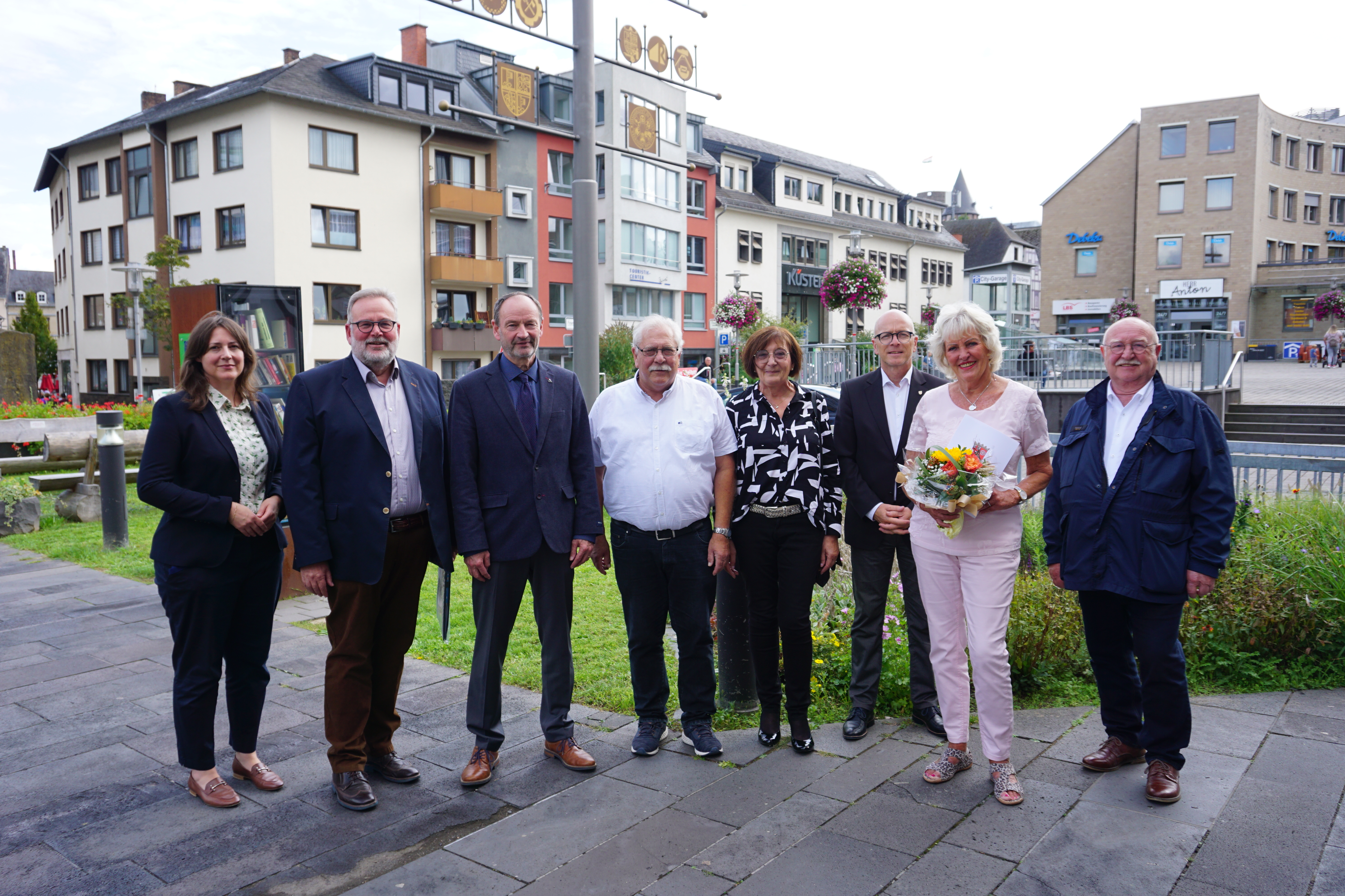 8 Personen stehe vor dem Rathaus - eine Dame hält einen Strauß Blumen in den Händen