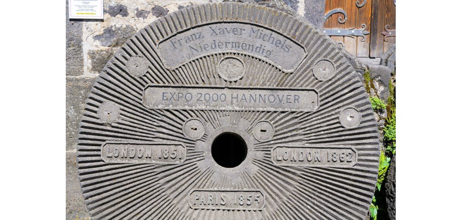 Der weitgereiste Mühlstein von Franz Xaver Michels aus Niedermendig war schon als Zeitzeuge auf verschiedenen Weltausstellungen Mühlstein mit verschiedenen Aufschriften drauf