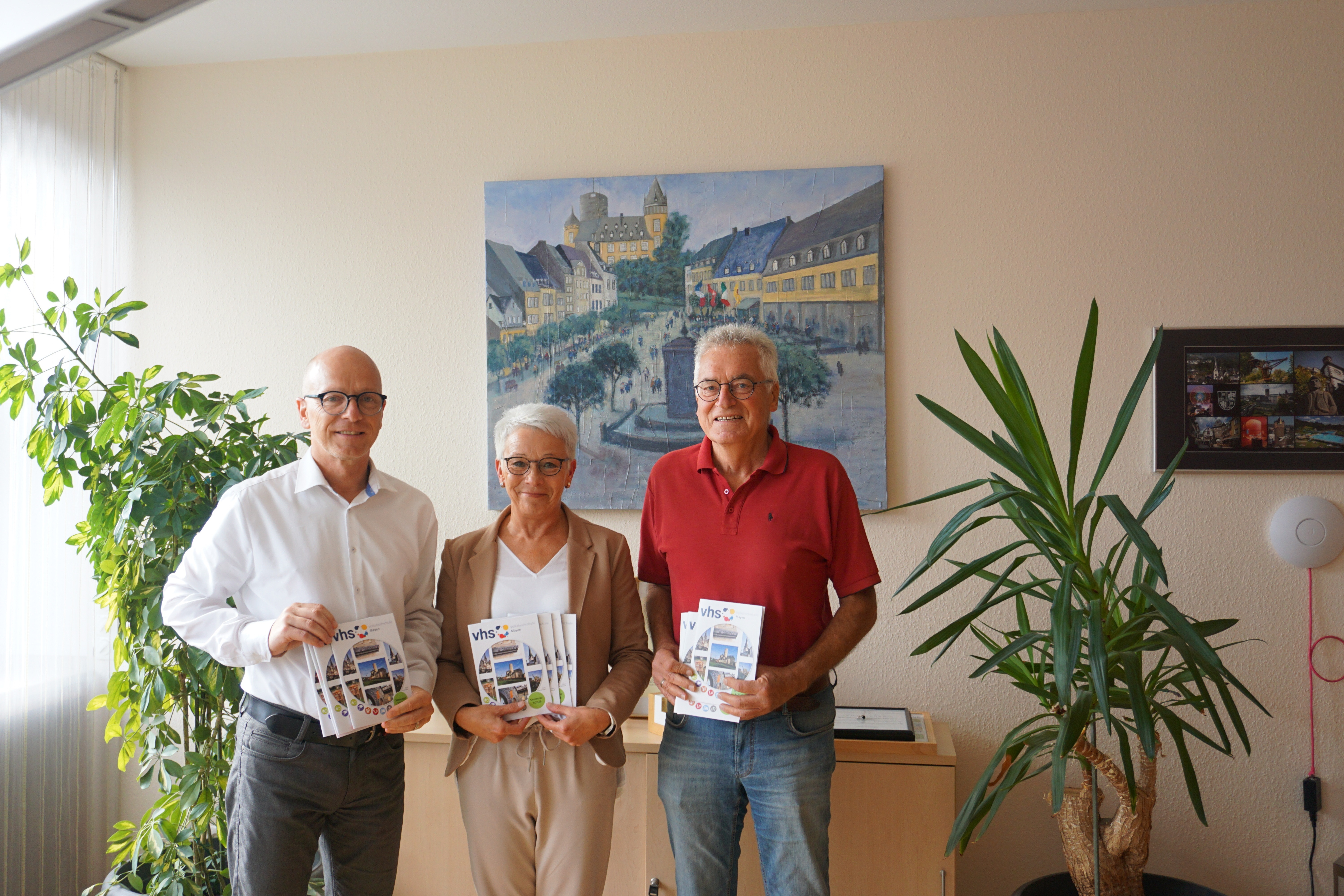3 Personen stehen für ein Bild zusammen und halten ein Heft in den Händen