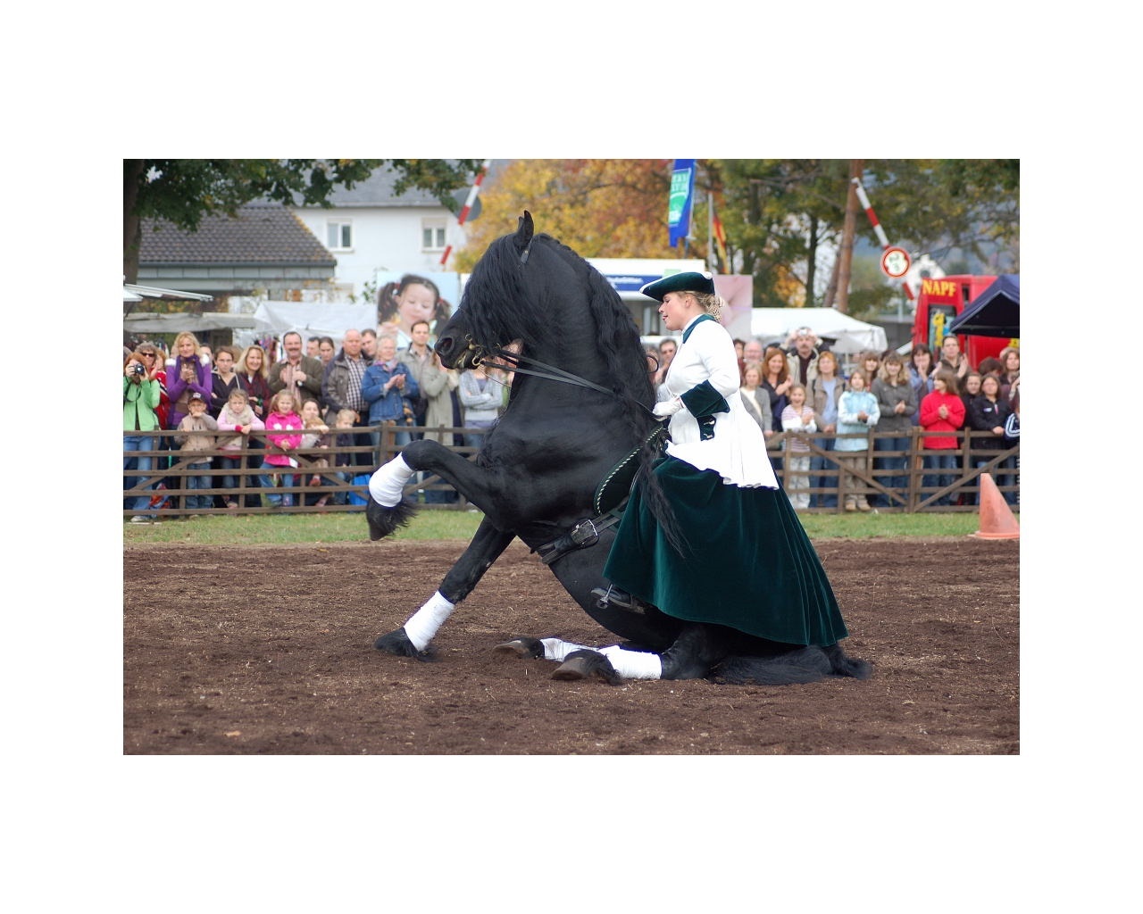 Frau in einem Kleid sitzt auf einem schwarzen Pferd, welches mit den Hinterbeinen auf dem Boden sitzt