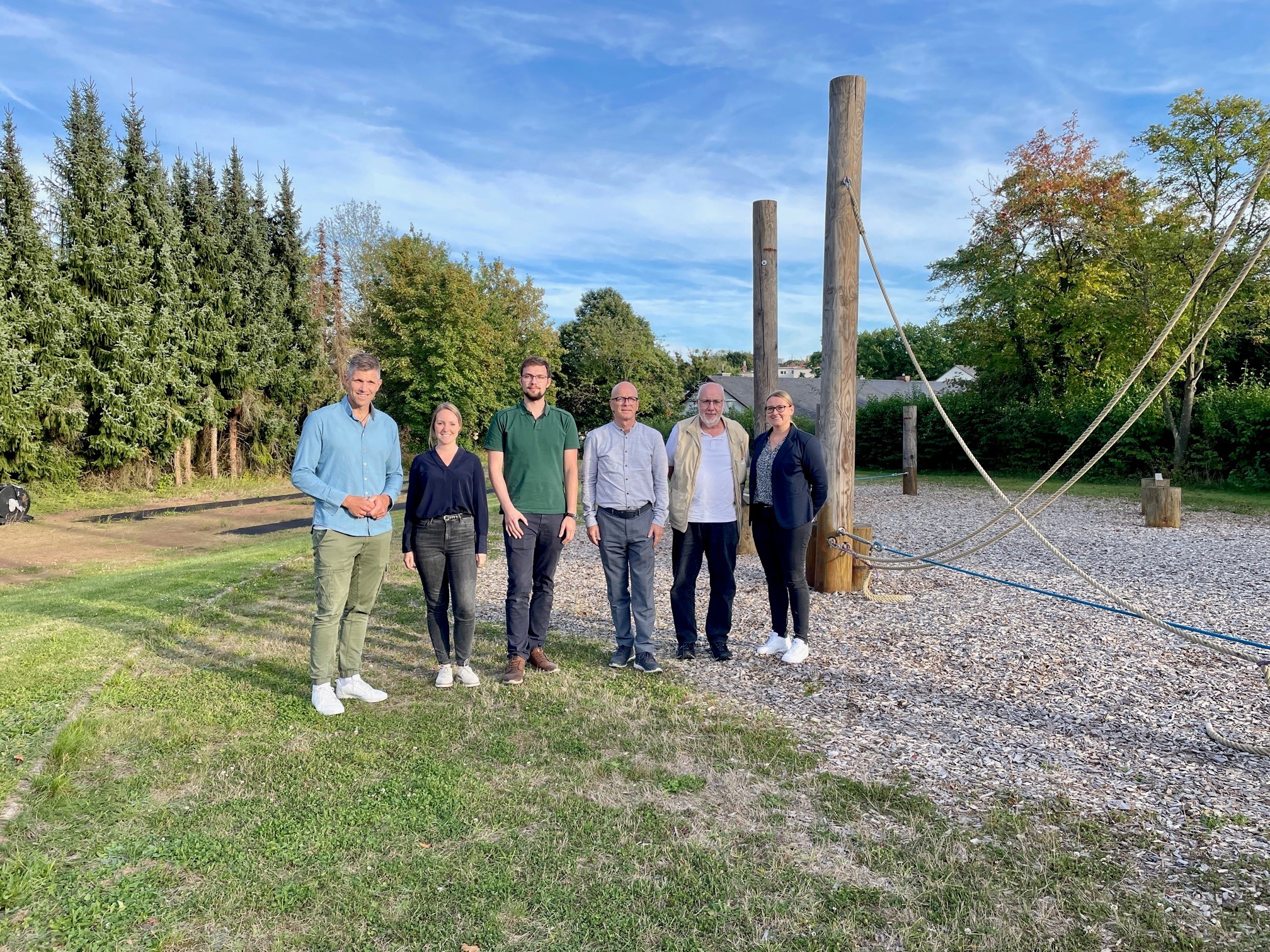 6 Personen stehen neben einem Niedrigseilparcours für ein Bild zusammen