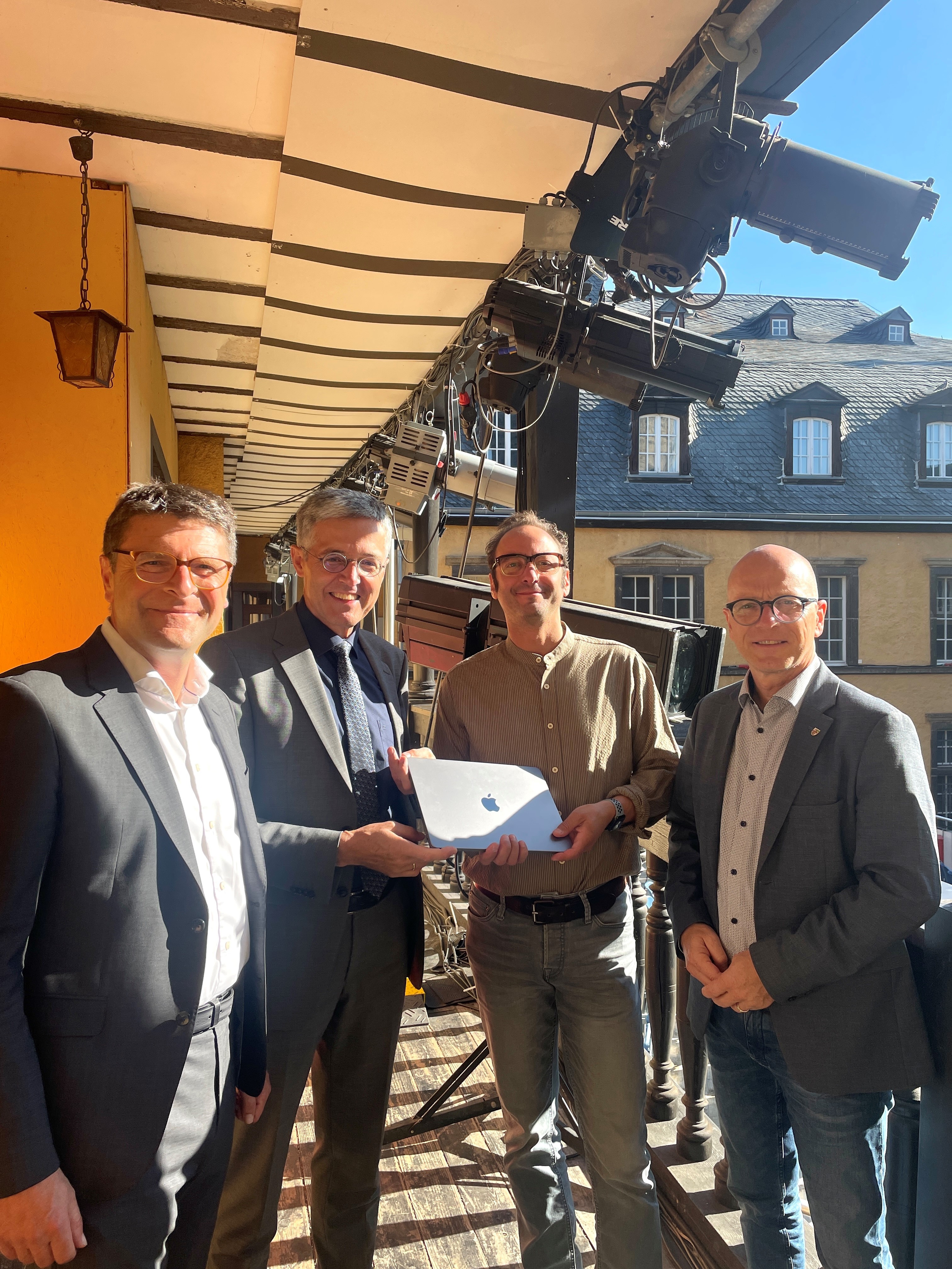 4 Personen stehen zusammen und halten ein MacBook in den Händen