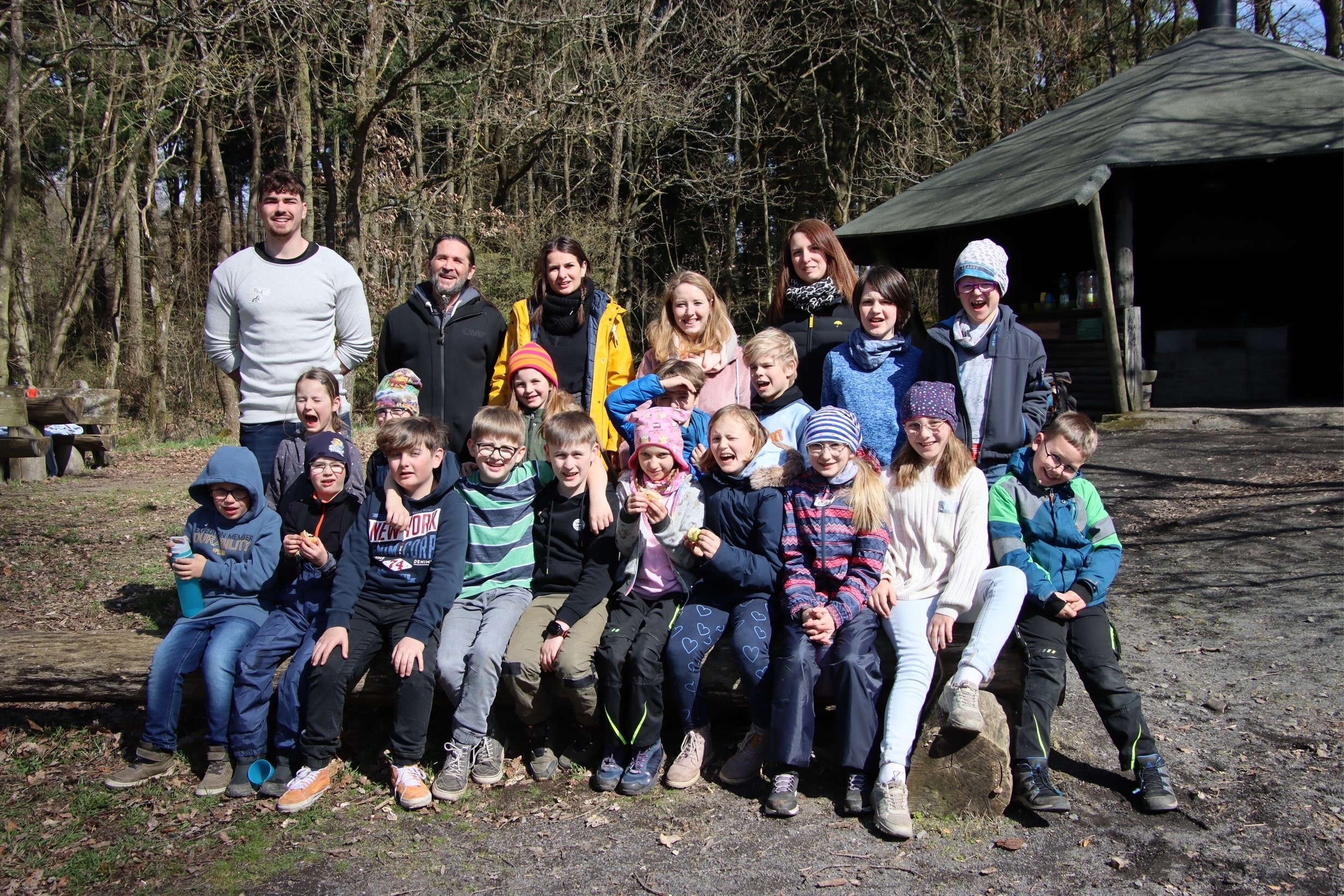 Kinder sitzen vor einer Waldhütte für ein Bild zusammen 