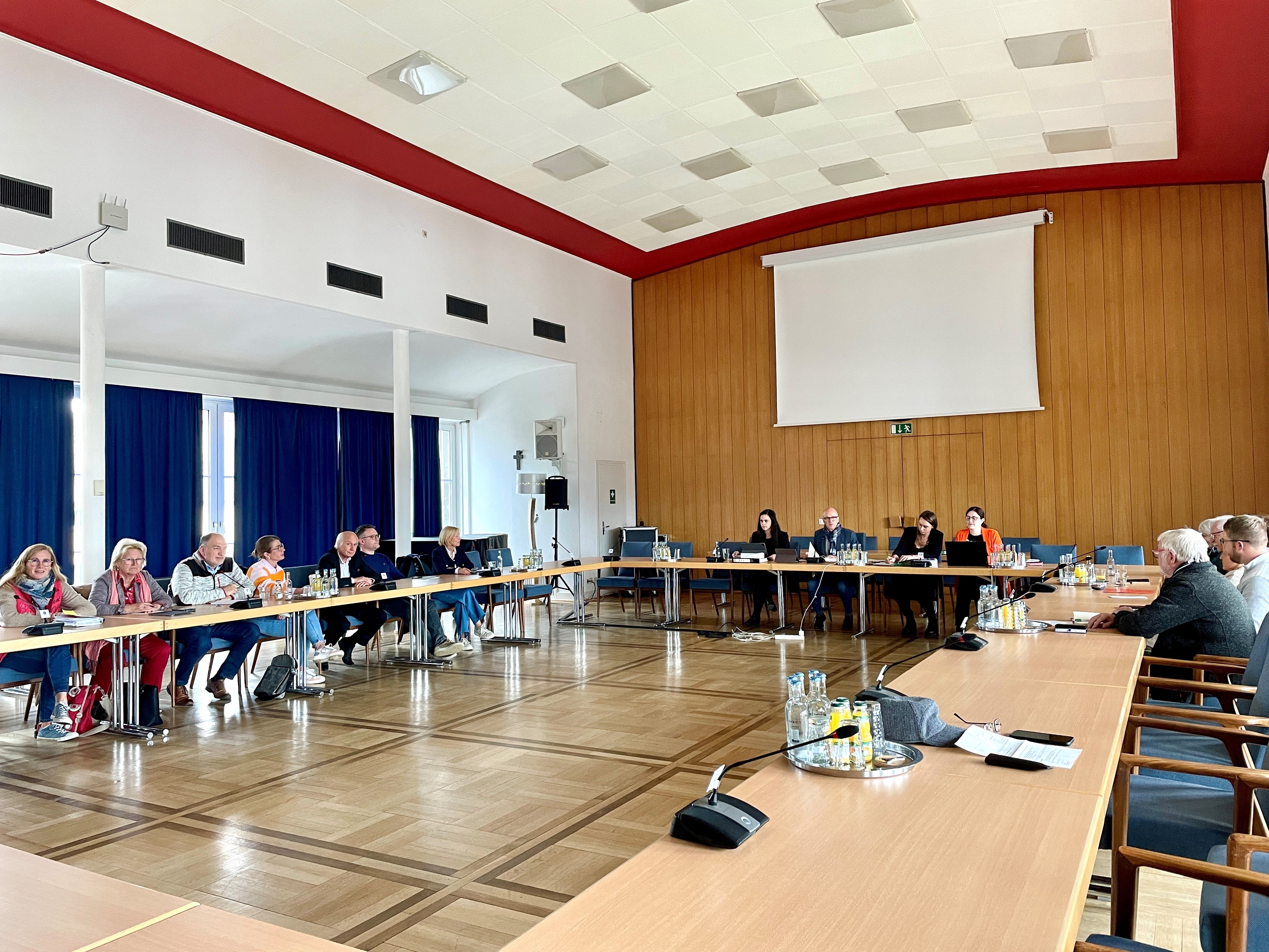 Mehrere Personen sitzen im Sitzungssaal und beraten sich