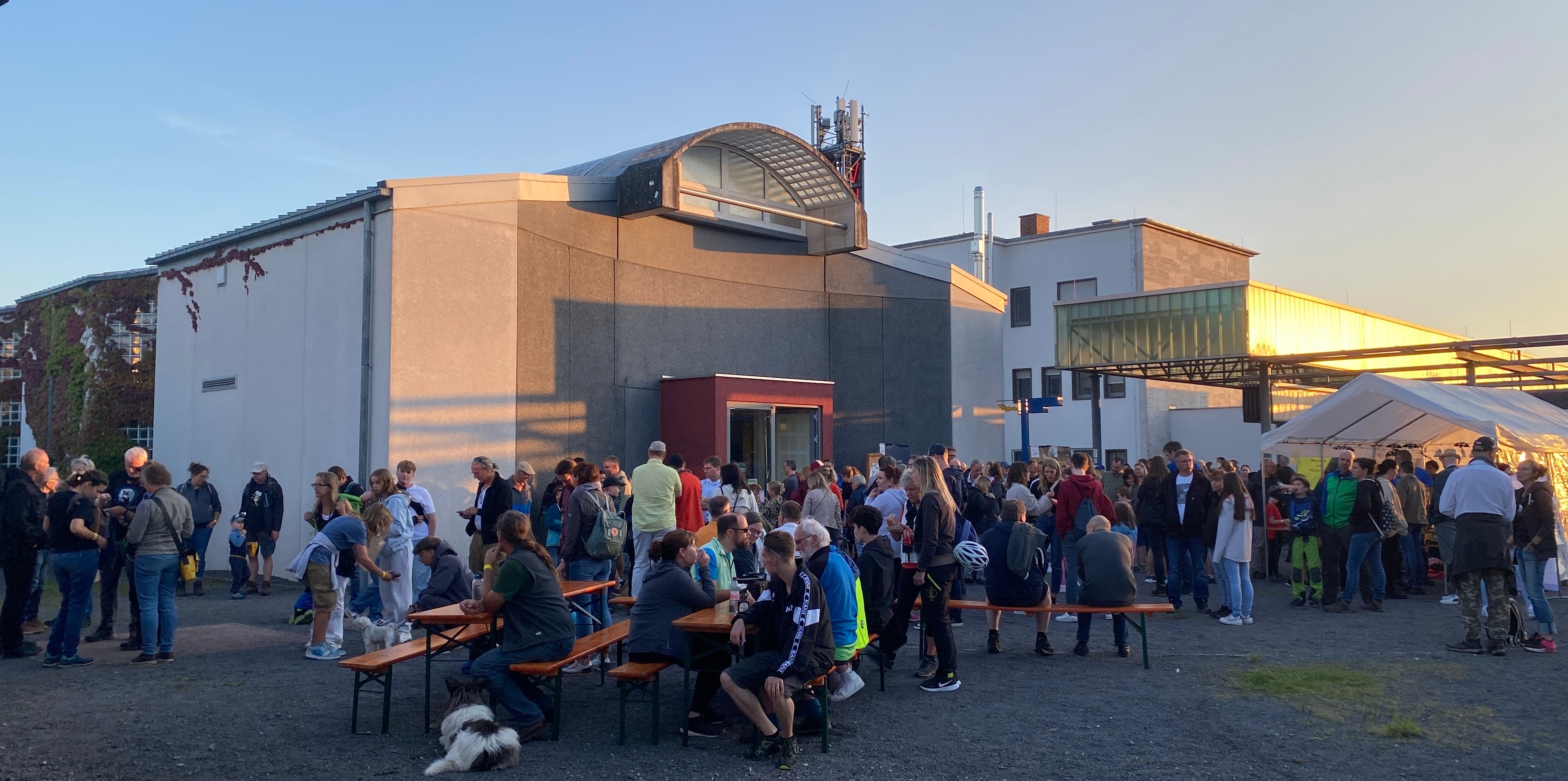 Viele Menschen auf Bänken im Innenhof der Erlebniswelten Grubenfeld. Die Sonne geht unter. 