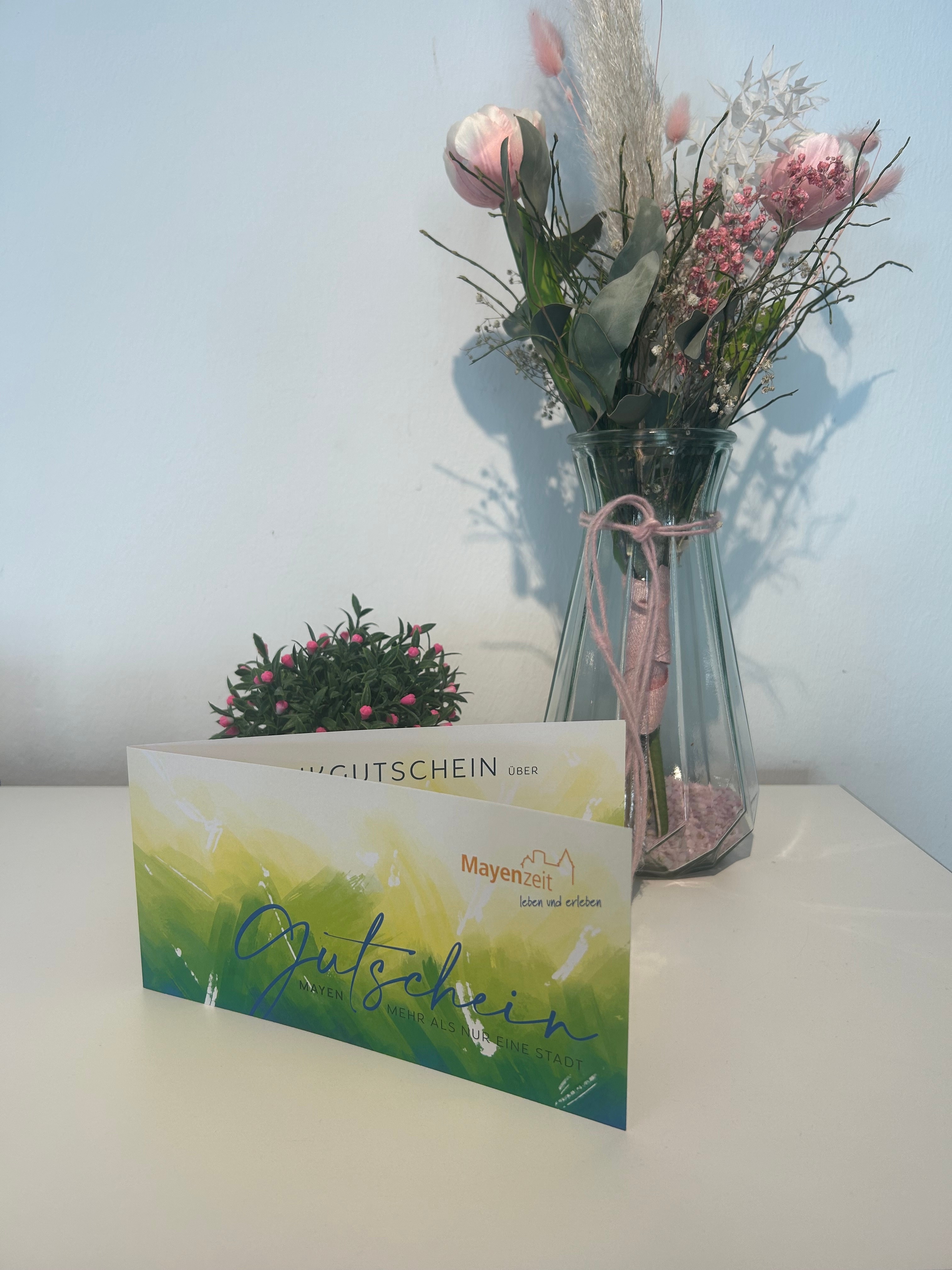 Mayen-Gutschein auf einem Tisch - im Hintergrund eine Pflanze