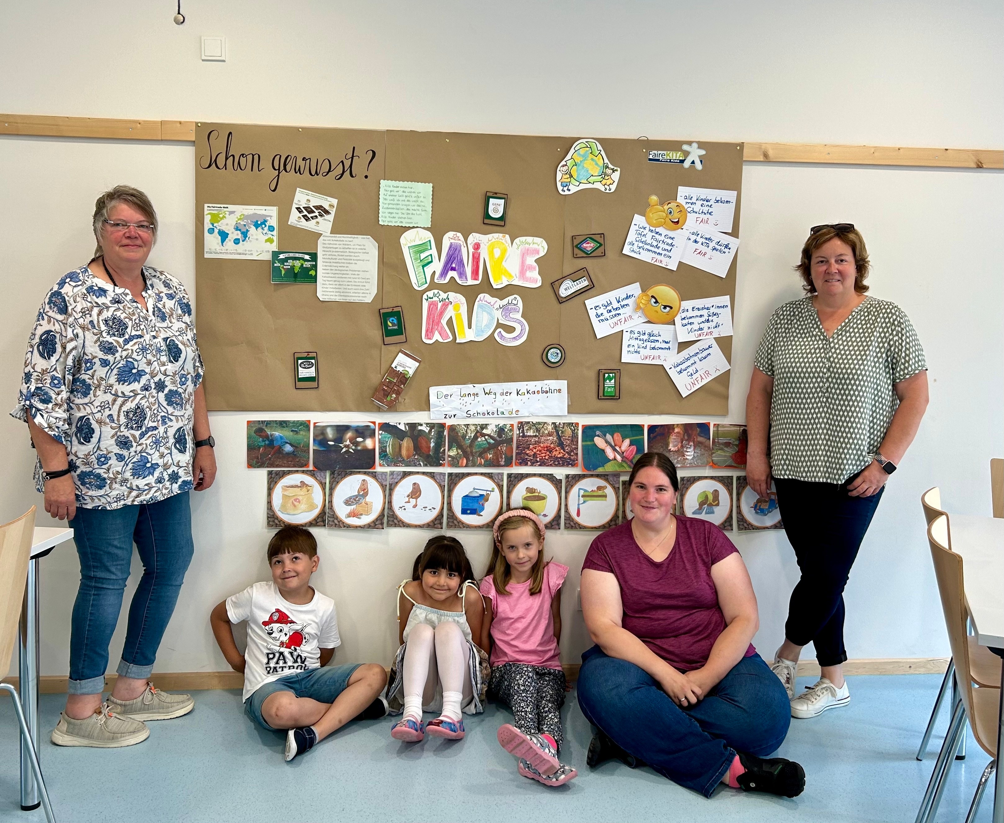 3 Erwachsene und 3 Kinder vor einem großen Plakat