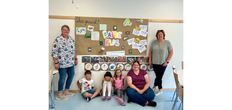 3 Erwachsene und 3 Kinder vor einem großen Plakat