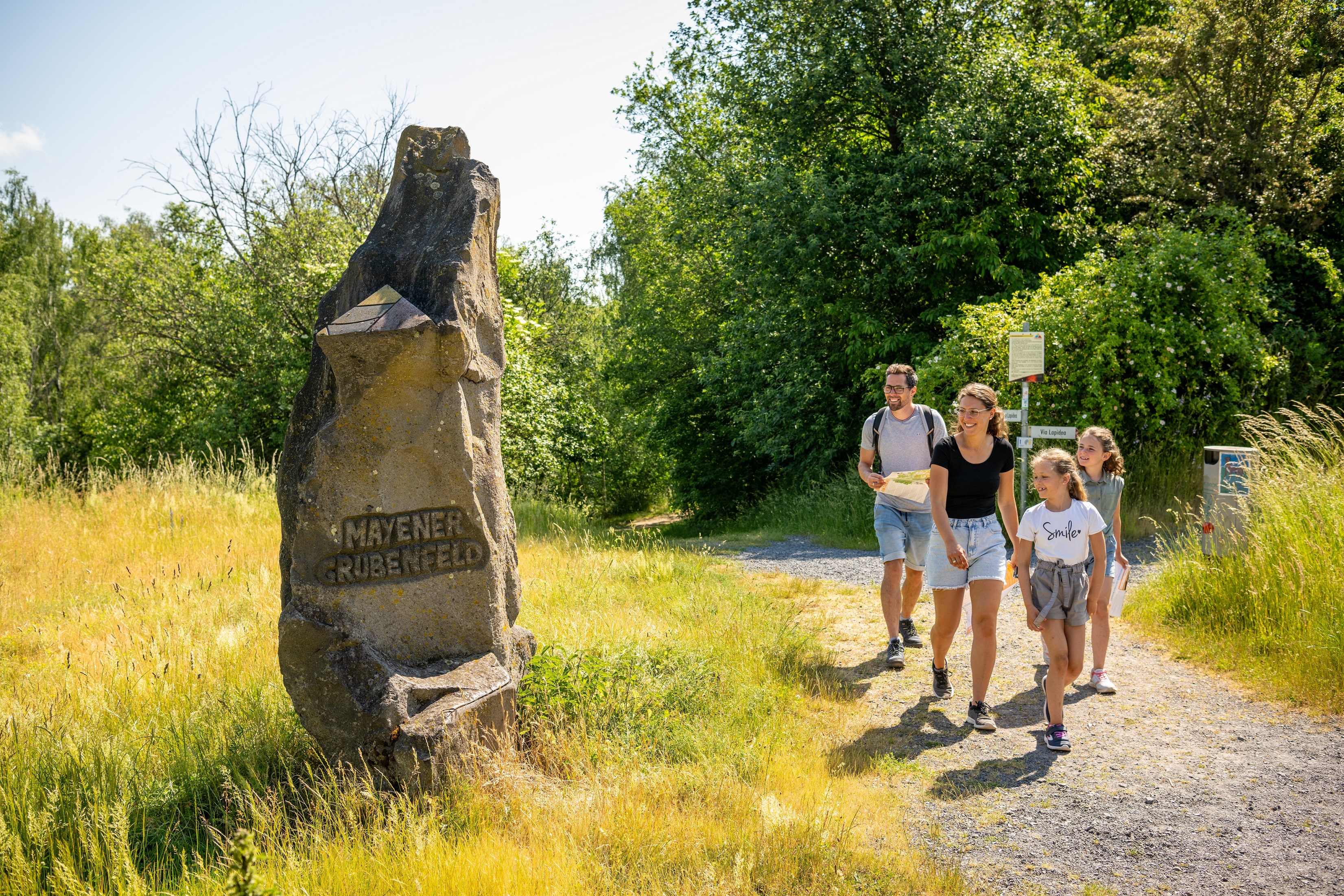 Familie läuft an einem Stein vorbei, worauf steht "Mayener Grubenfeld"