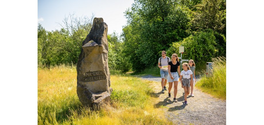 Familie läuft an einem Stein vorbei, worauf steht "Mayener Grubenfeld"