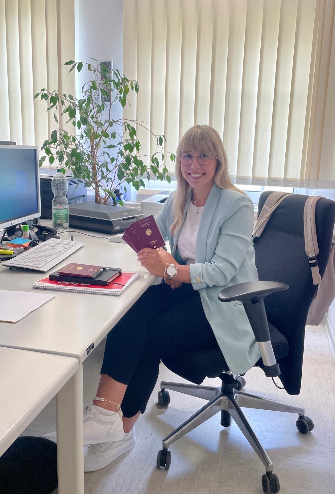 Frau sitzt am Schreibtisch und hält Reisepässe an der Hand