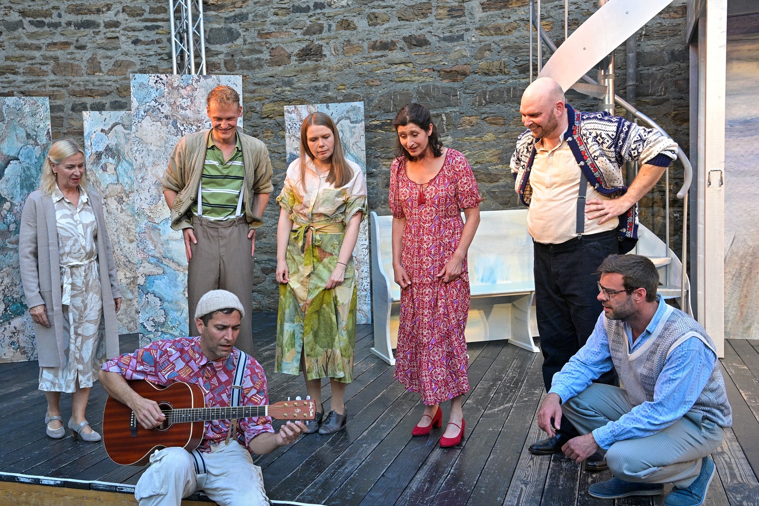 7 Personen auf einer Bühne - einer spielt sitzende Gitarre