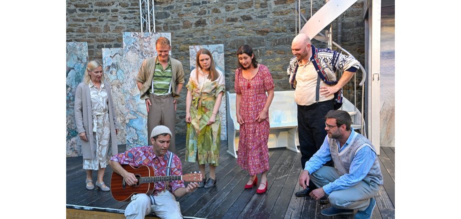 7 Personen auf einer Bühne - einer spielt sitzende Gitarre