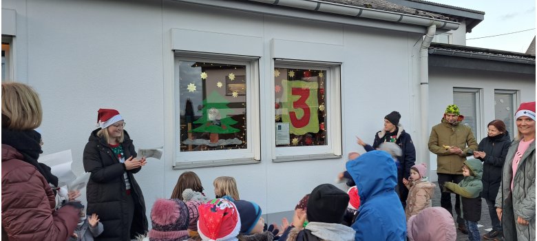 Ein weiteres Adventsfenster wird besucht Mehrere Erwachsene und Kinder stehen vor einem geschmückten Fenster