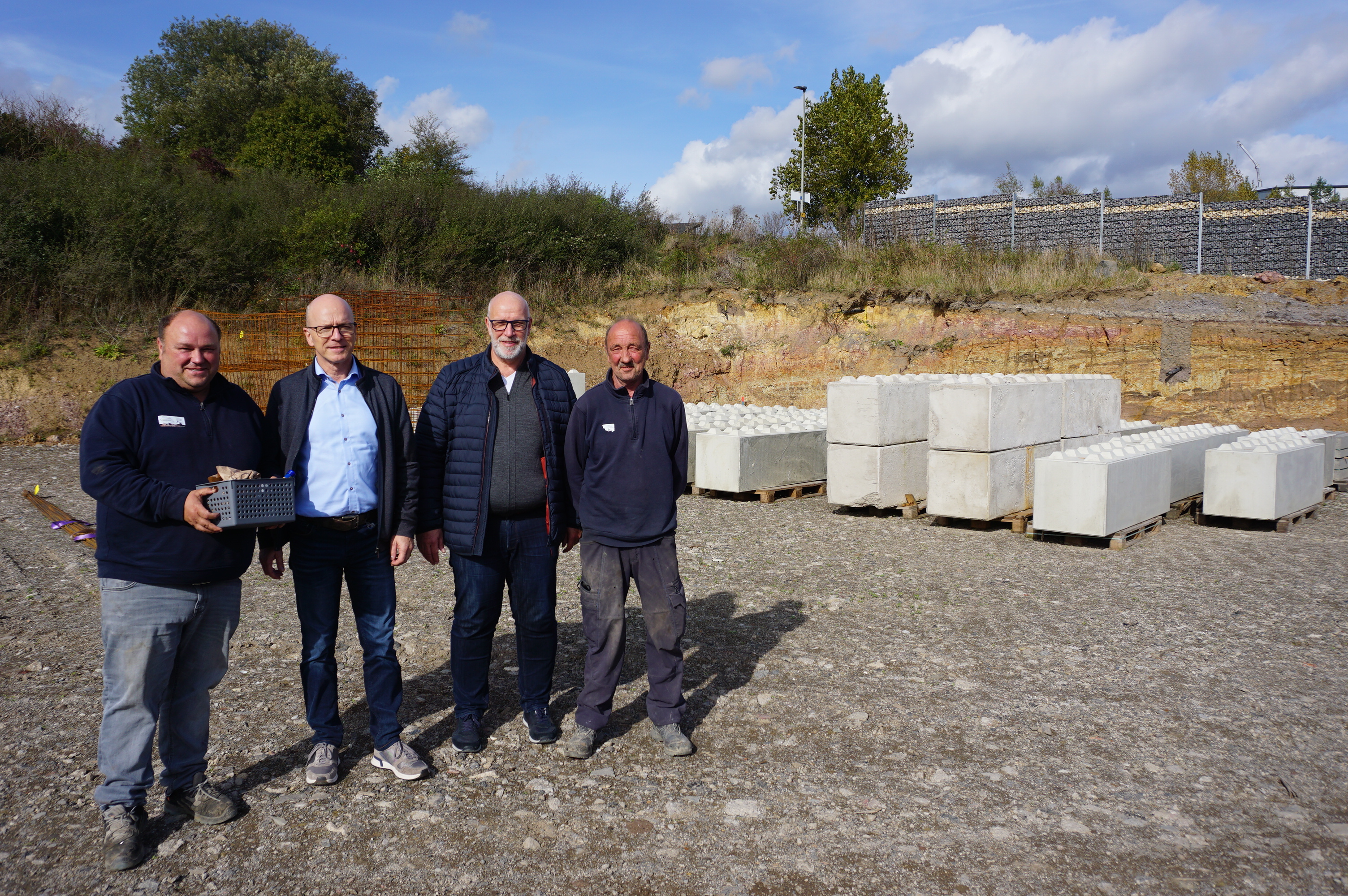 4 Personen auf dem Gelände der Firma. Im Hintergrund sind Baumaterialien zu sehen