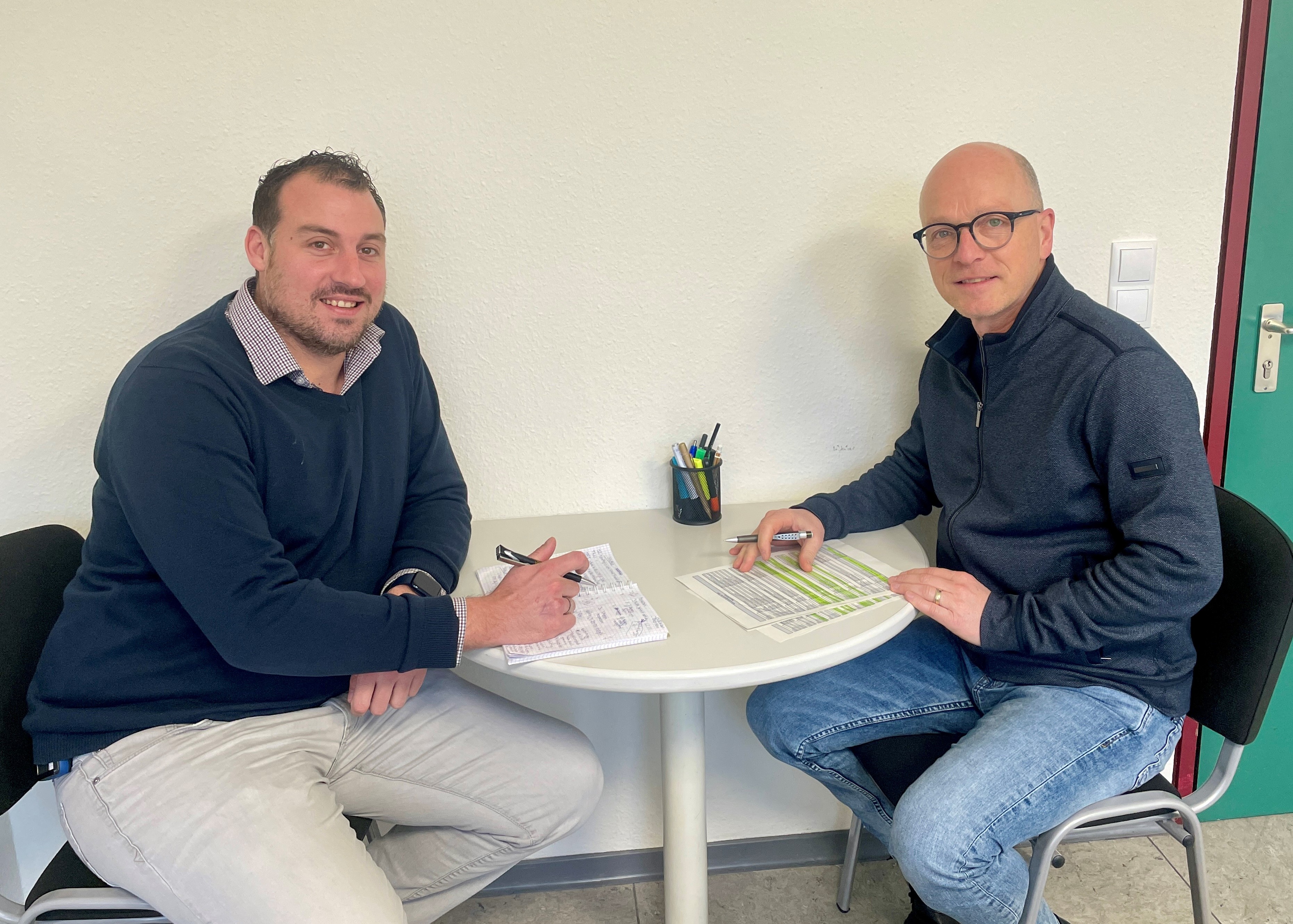 2 Männer sitzen mit Unterlagen an einem Tisch