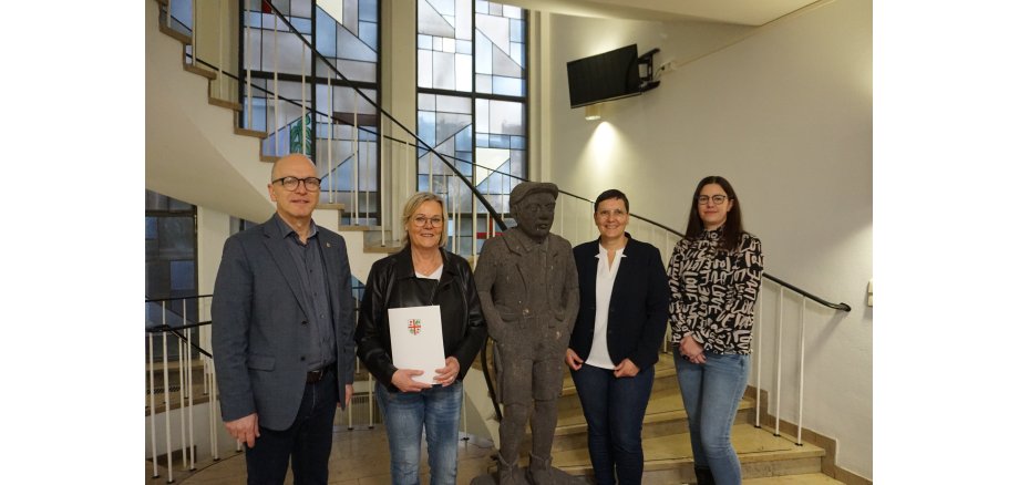 v.l.n.r.: Oberbürgermeister Dirk Meid, Andrea Herrmann, Mitarbeiterin Personalabteilung Heike Ritzdorf und stellv. Personalratsvorsitzende Svenja Schäfges-Zimmer 4 Personen stehen um eine Steinfigur vor einer Treppe zusammen - eine Frau hält eine Urkunde in der Hand
