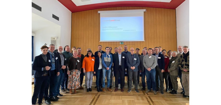 Gruppe von Menschen stehen vor einer großen Leinwand zu einem Foto zusammen