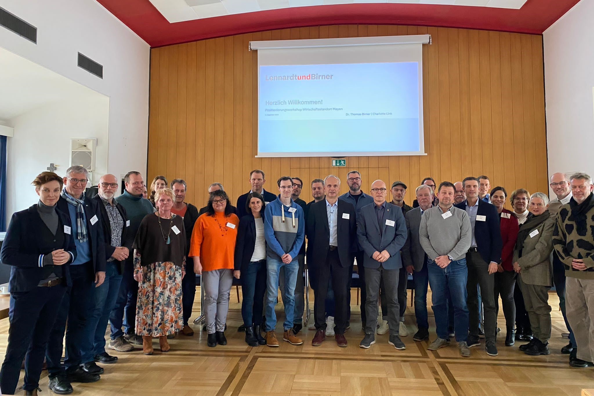 Gruppe von Menschen stehen vor einer großen Leinwand zu einem Foto zusammen