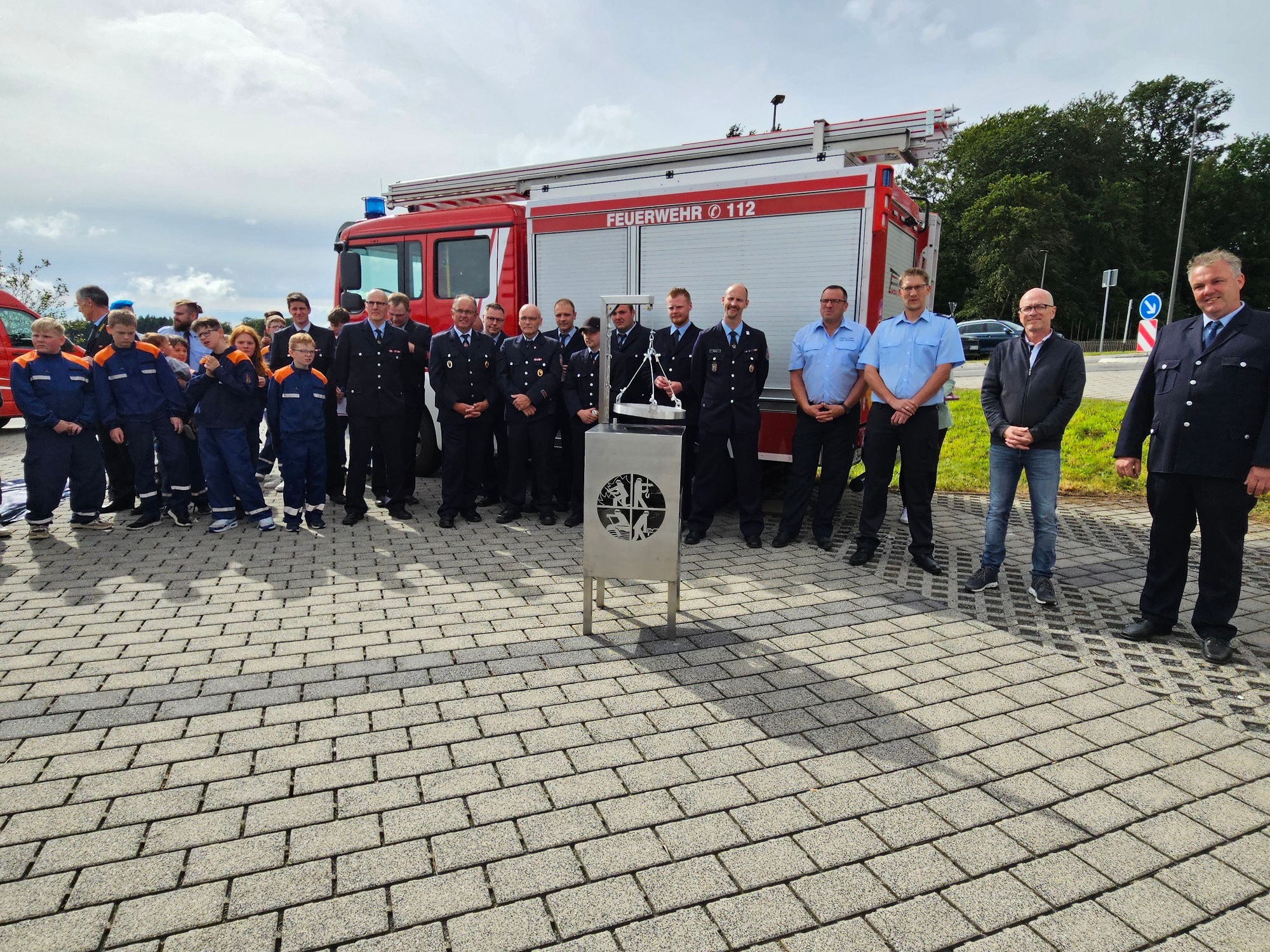 Die Freiwillige Feuerwehr der Stadt Mayen Löscheinheit Kürrenberg bei ihrem Appell Eine Gruppe von Menschen steht vor einem Feuerwehrfahrzeug im Halbkreis. Im Vordergrund ein Grill