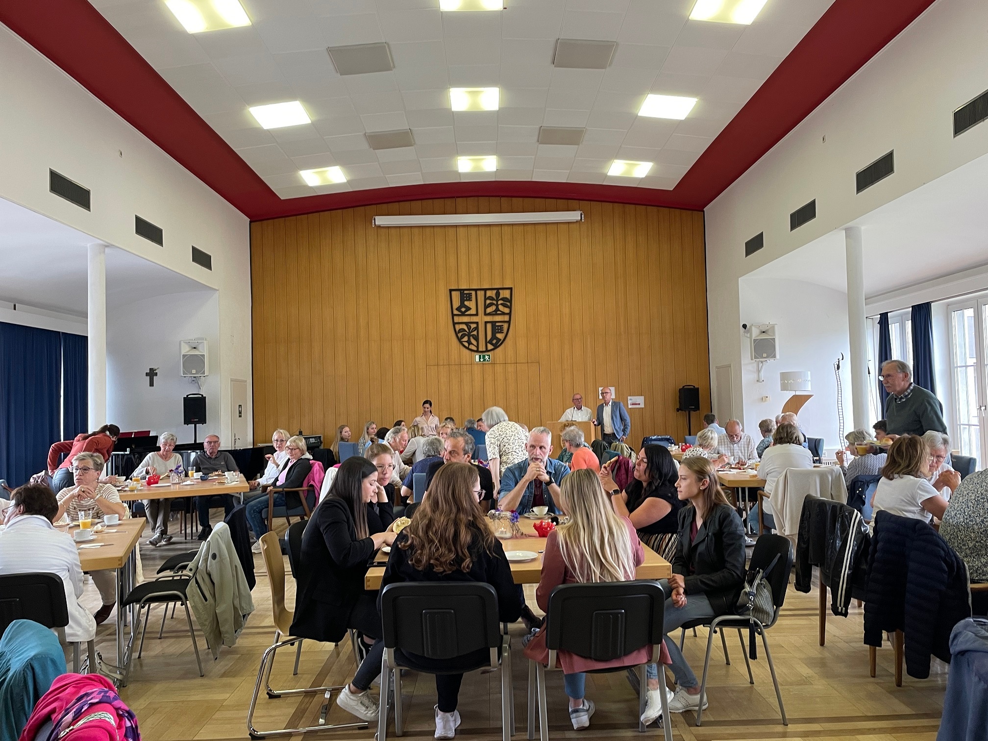 Ein voll besetzter Sitzungssaal -  Menschen sitzen am Tisch und essen