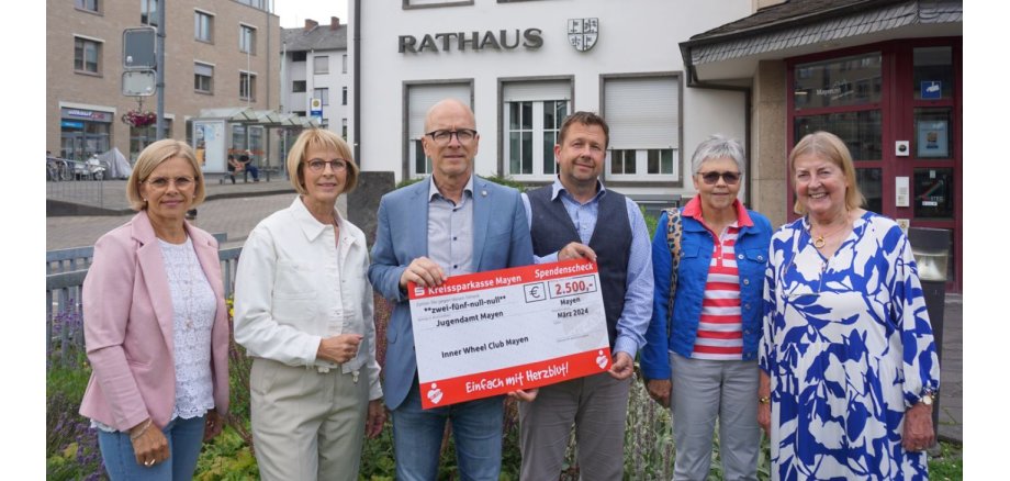 Sechs Personen mit Spendenscheck vor dem Rathaus