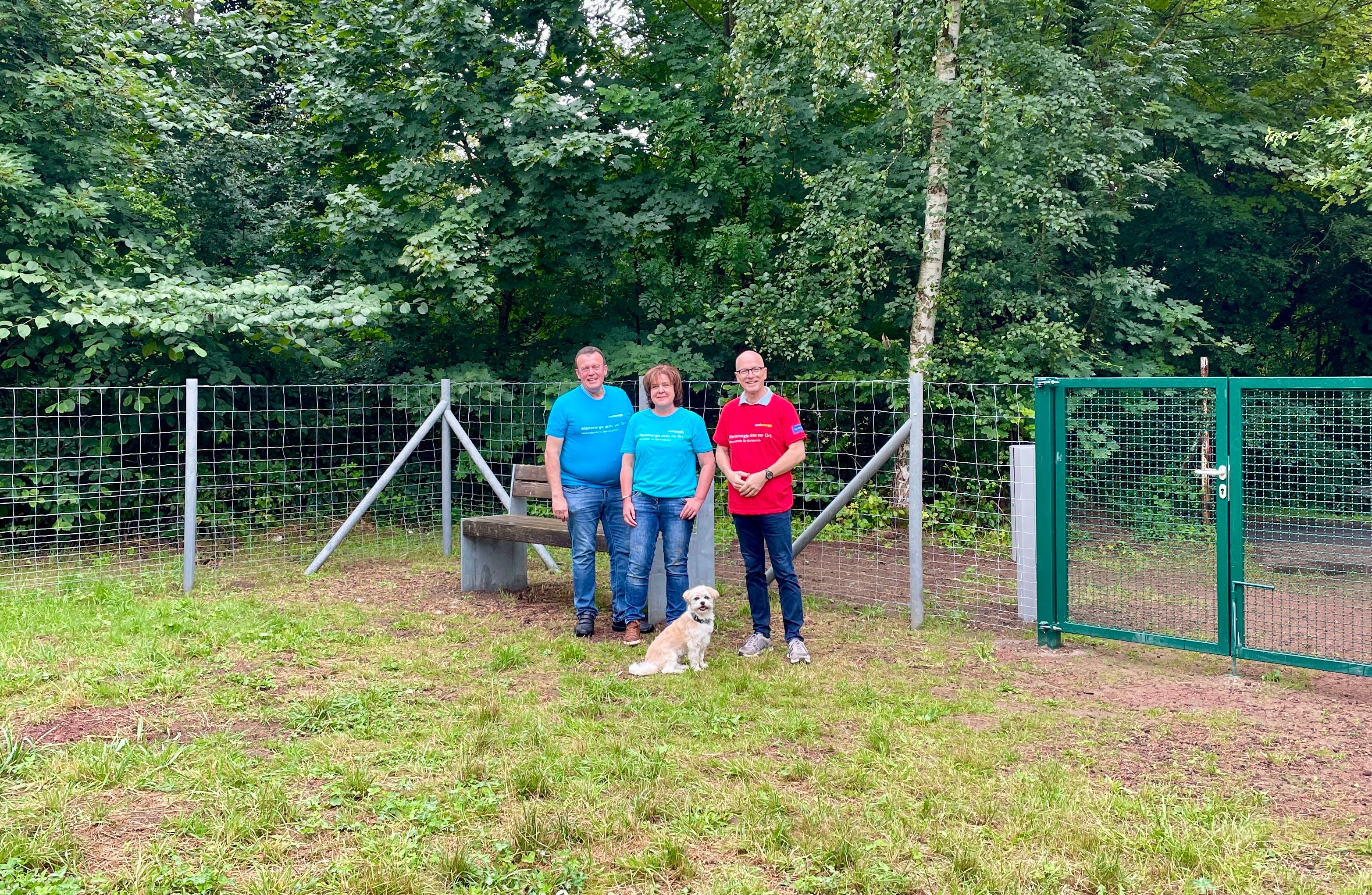 3 Personen stehe auf einem Rasen vor einem Zaun