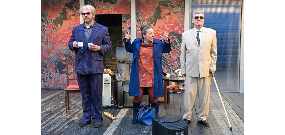 Zwei Männer mit Sonnenbrille und eine Frau in der Mitte stehen auf einer Bühne