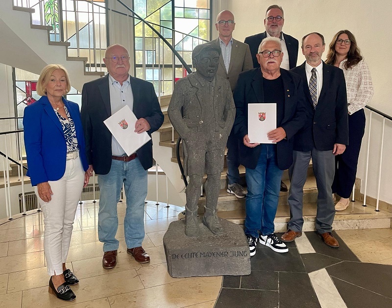 7 Personen stehen im Eingangsbereich des Rathauses  - in der Mitte der Mayener Jung aus Stein