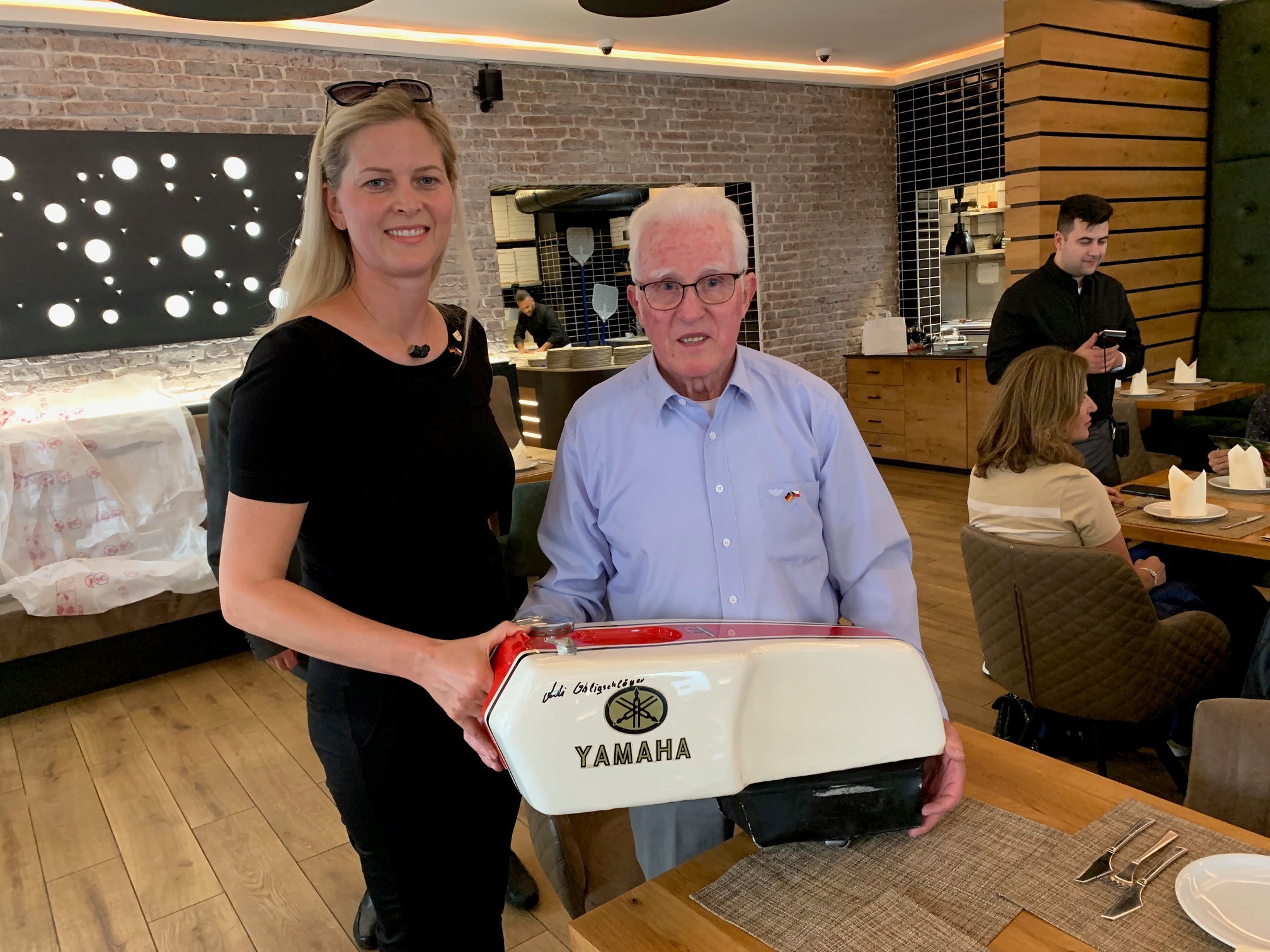 Eine Frau und ein Mann mit einem Tank eines Motorrades in den Händen