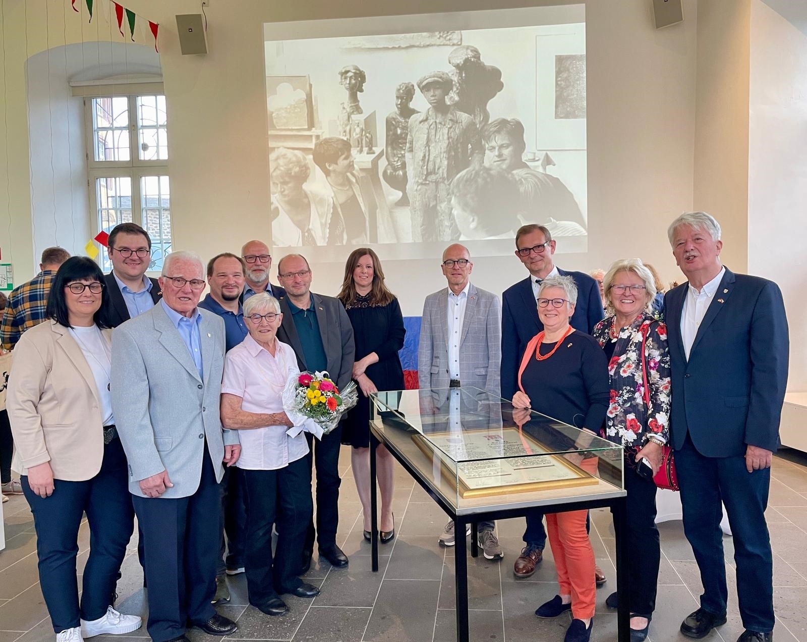 Mehrere Personen stehen um einen Glaskasten - im Hintergrund ein Bild in schwarz-weiß