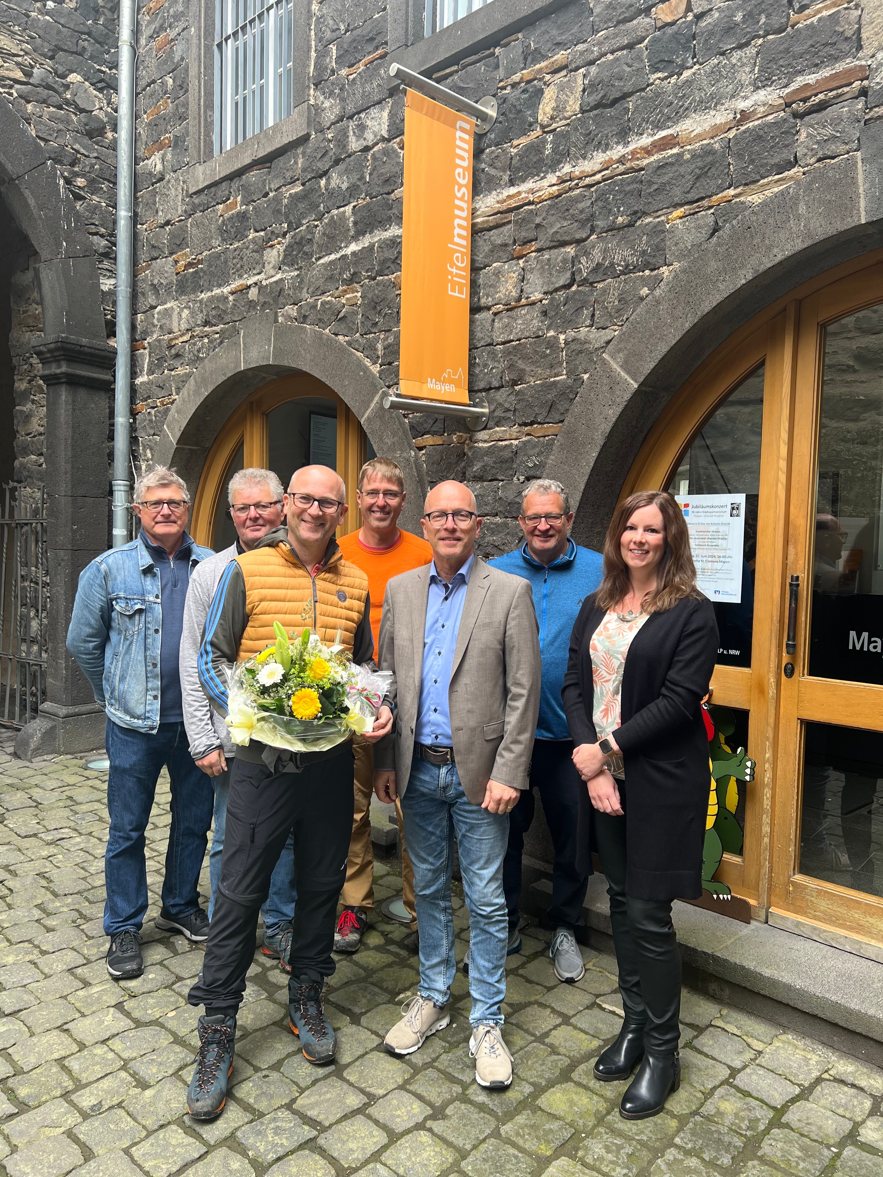 Sieben Personen stehen vor dem Eingang des Eifelmuseums - einer hält einen Blumenstrauß in den Händen