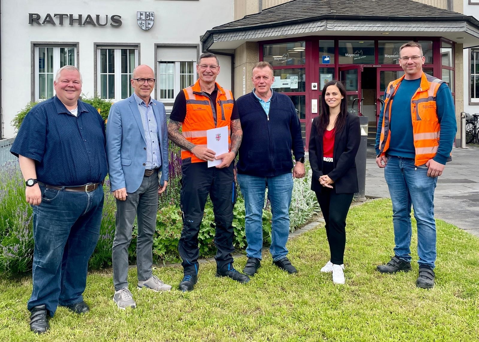 6 Personen stehen vor dem Rathaus für ein Foto zusammen - einer hält eine Urkunde in den Händen