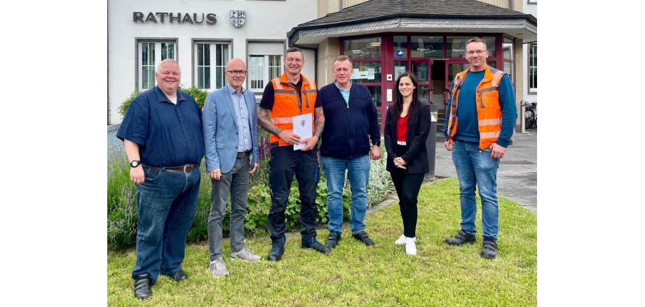 6 Personen stehen vor dem Rathaus für ein Foto zusammen - einer hält eine Urkunde in den Händen
