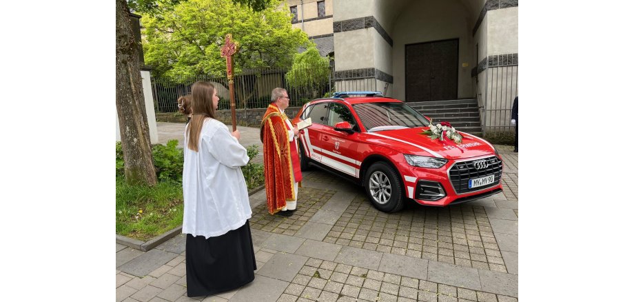 Pastor segnet einen Wagen ein, da neben steht eine Messdienerin