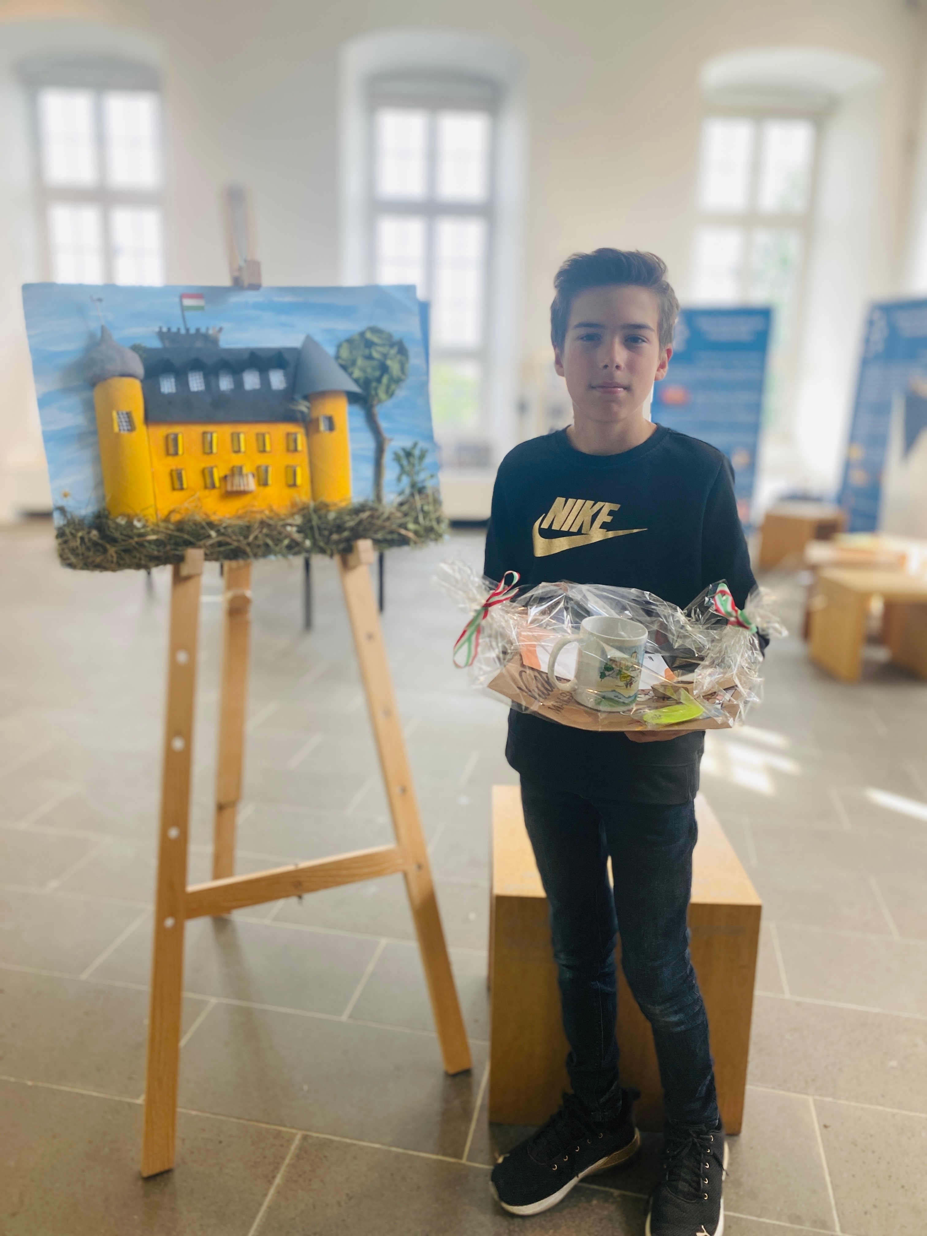 Junge steht neben einem Kunstwerk und hält ein Präsent in den Händen