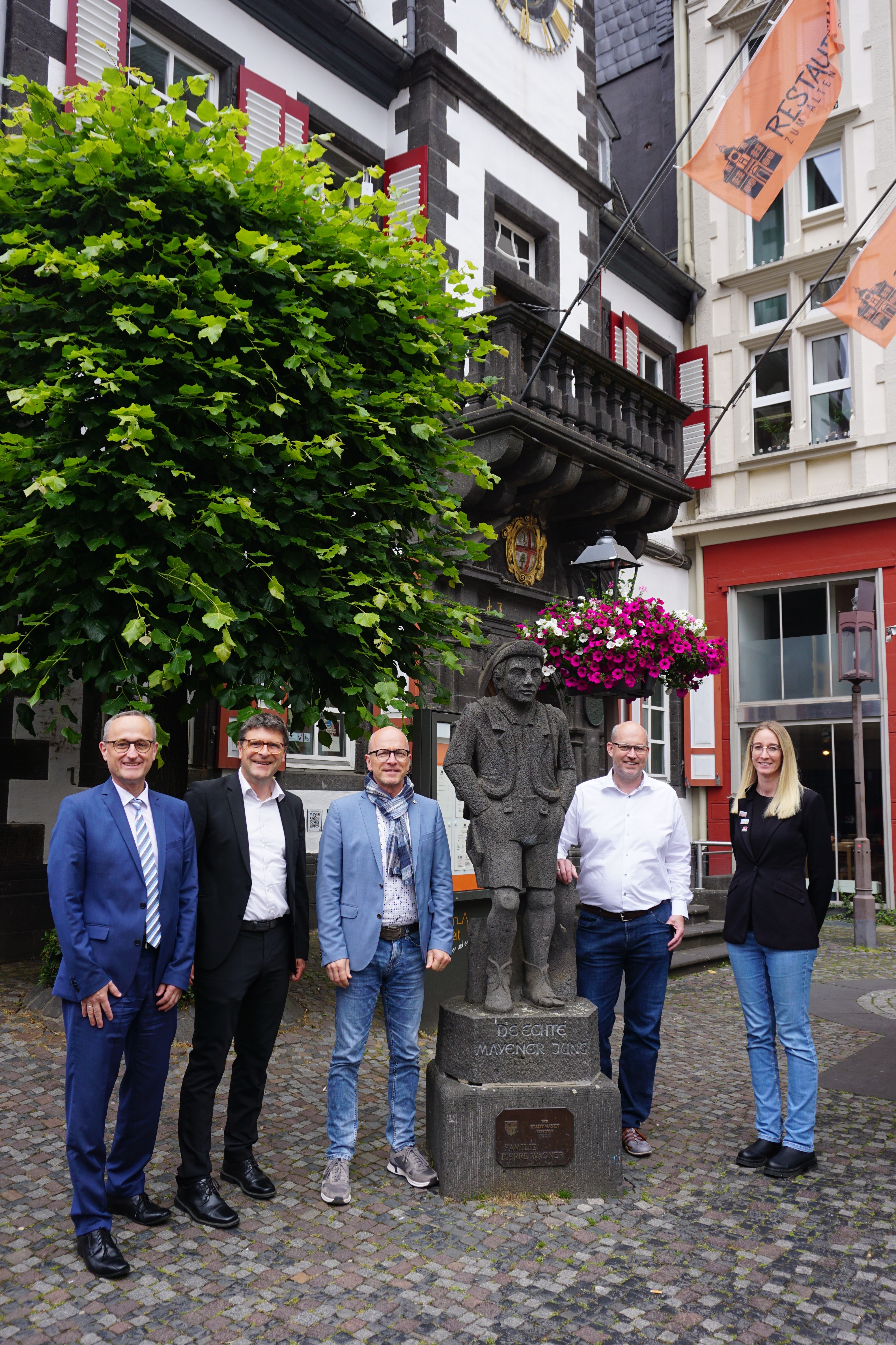 5 Personen stehen neben einer Steinfigur und vor einer Laterne mit Blumenampeln