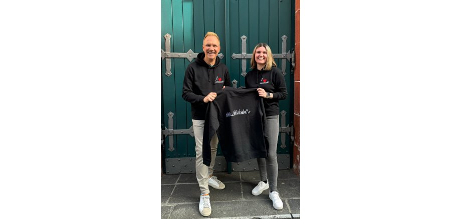 Eine Frau und ein Mann halten zusammen einen Pullover vor sich und präsentieren diesen