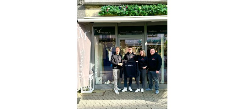 4 Personen stehen vor einem Laden und halten einen Pullover hoch