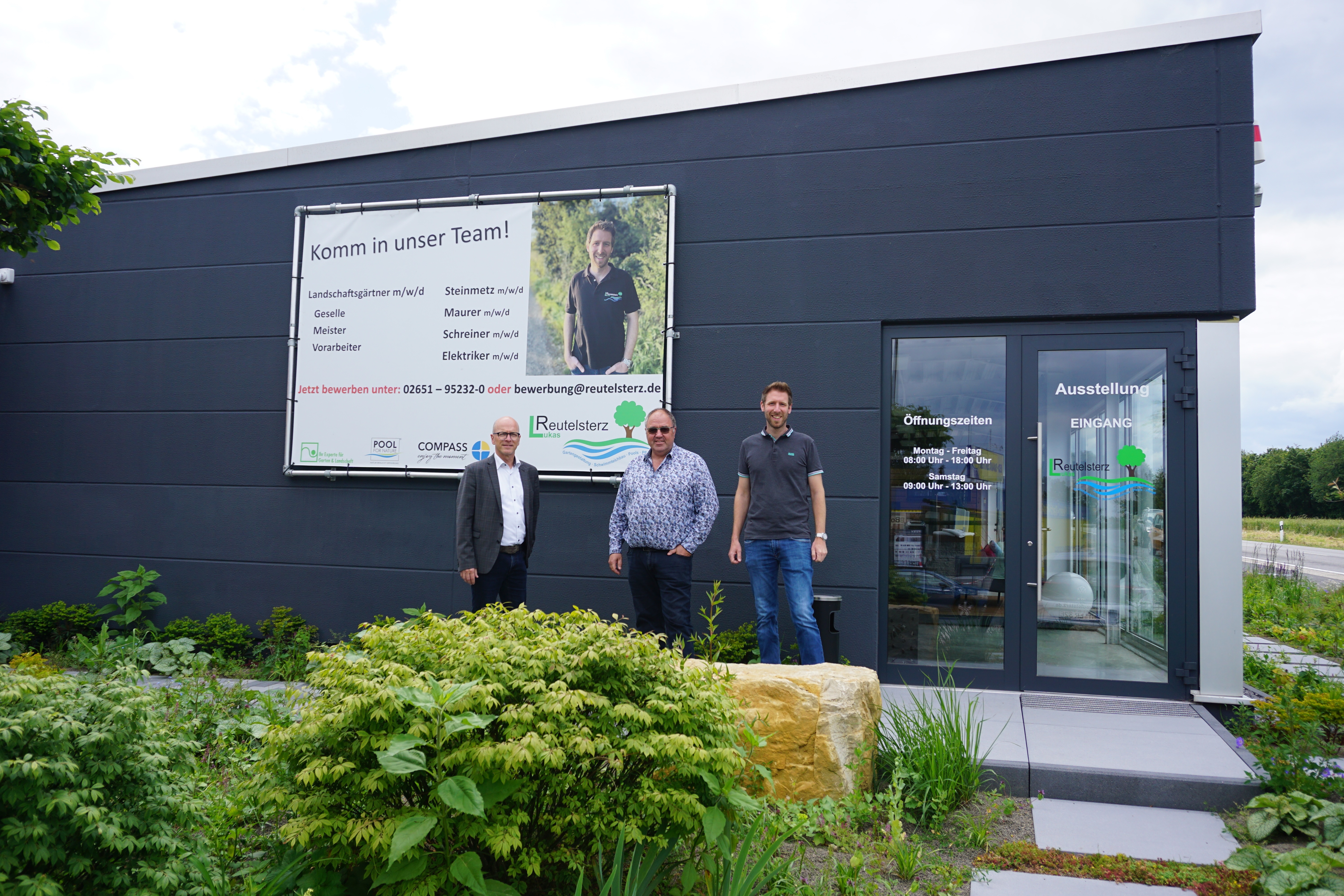 3 Personen stehe vor einem Werbebanner an einem Gebäude
