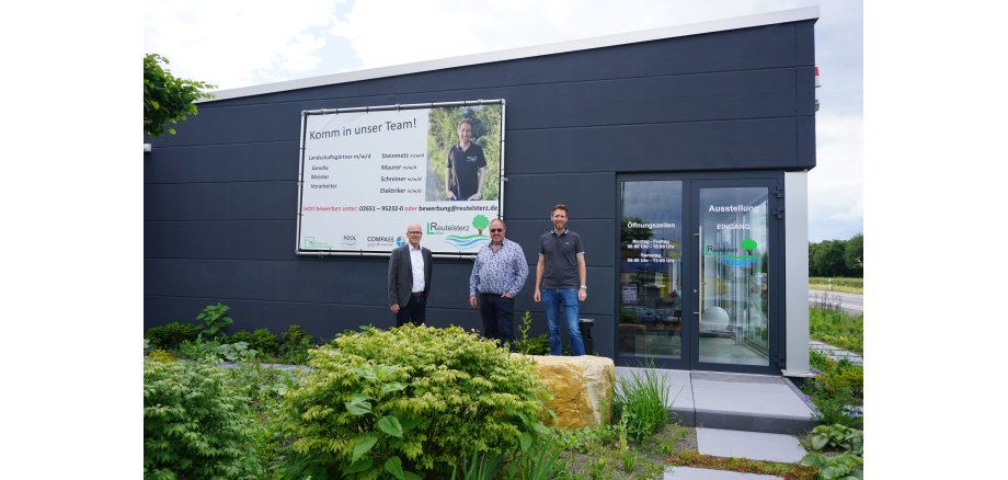 3 Personen stehe vor einem Werbebanner an einem Gebäude