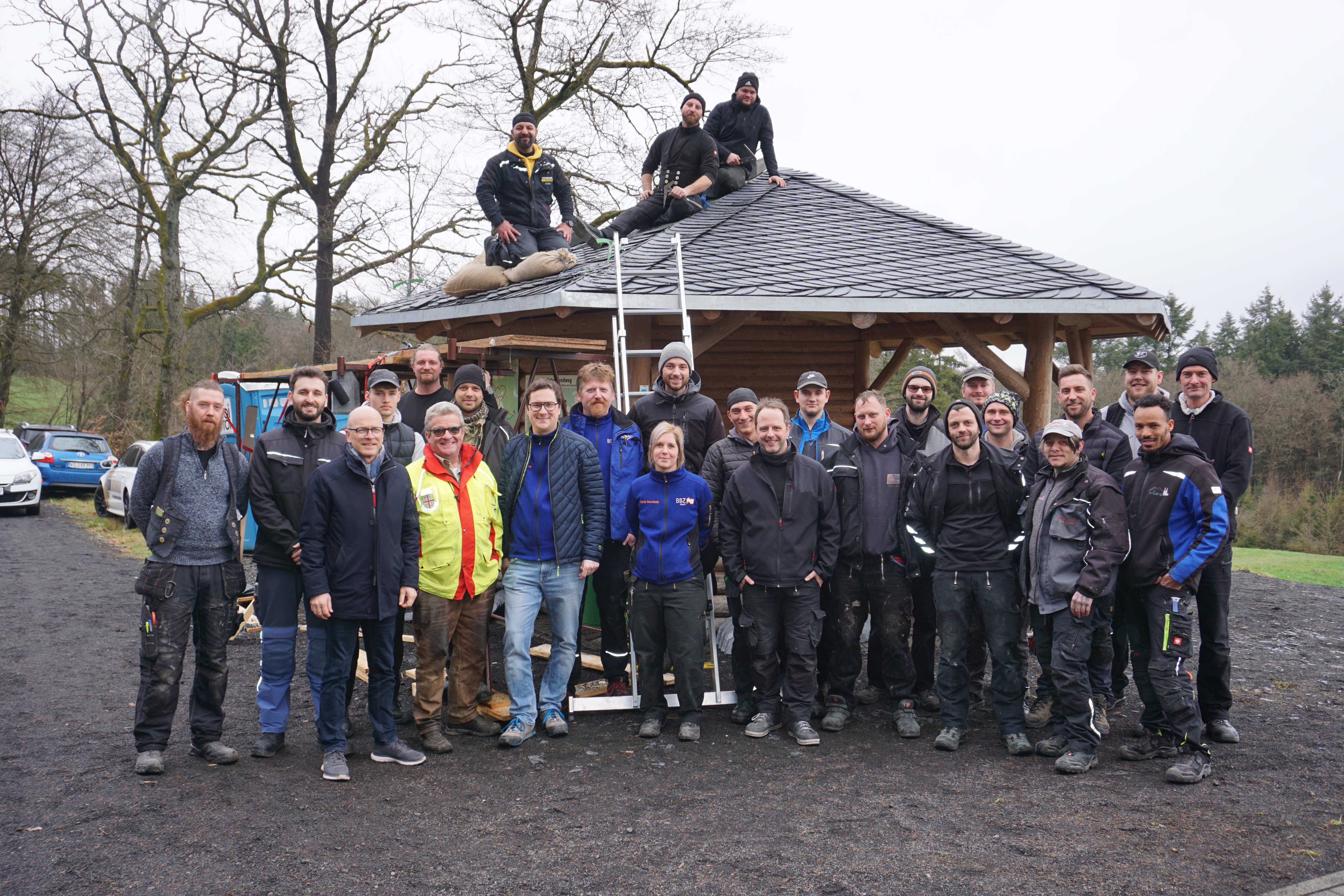 Dachdeckerinnen und Dachdecker stehen vor eine Hütte zu einem Bild zusammen