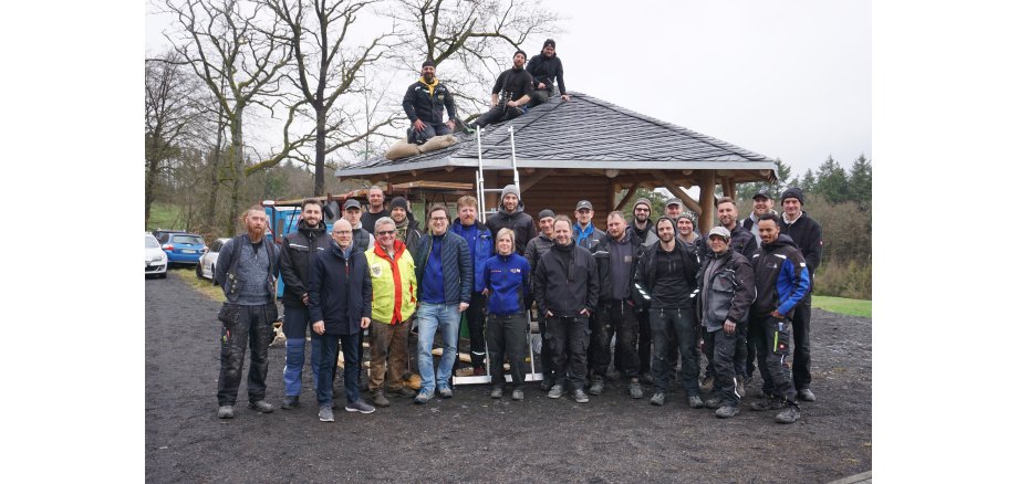 Dachdeckerinnen und Dachdecker stehen vor eine Hütte zu einem Bild zusammen