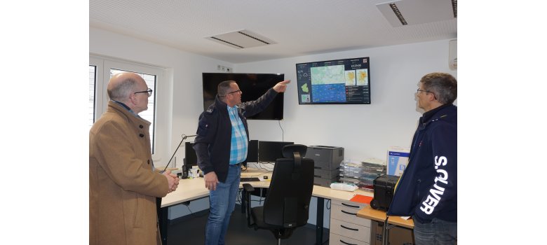 Thomas Velten erläutert die technische Ausstattung in der FEZ eine Person erklärt in der Einsatzzentrale etwas - 2 hören zu